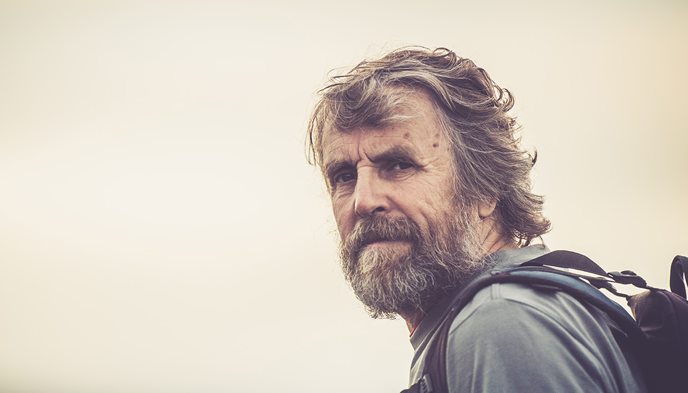 Ein älterer Mann, der einen Rucksack trägt, schaut in die Kamera.